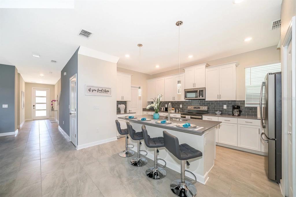 A modern kitchen features white cabinetry, a gray island with bar stools, and tile flooring — 2770 BOOKMARK DRIVE, KISSIMMEE, FL