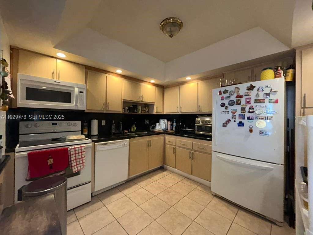 A kitchen features light wood cabinets, black countertops, white appliances, and beige tile flooring — 13499 Biscayne Blvd # 1206, North Miami FL 33181, NORTH MIAMI, FL
