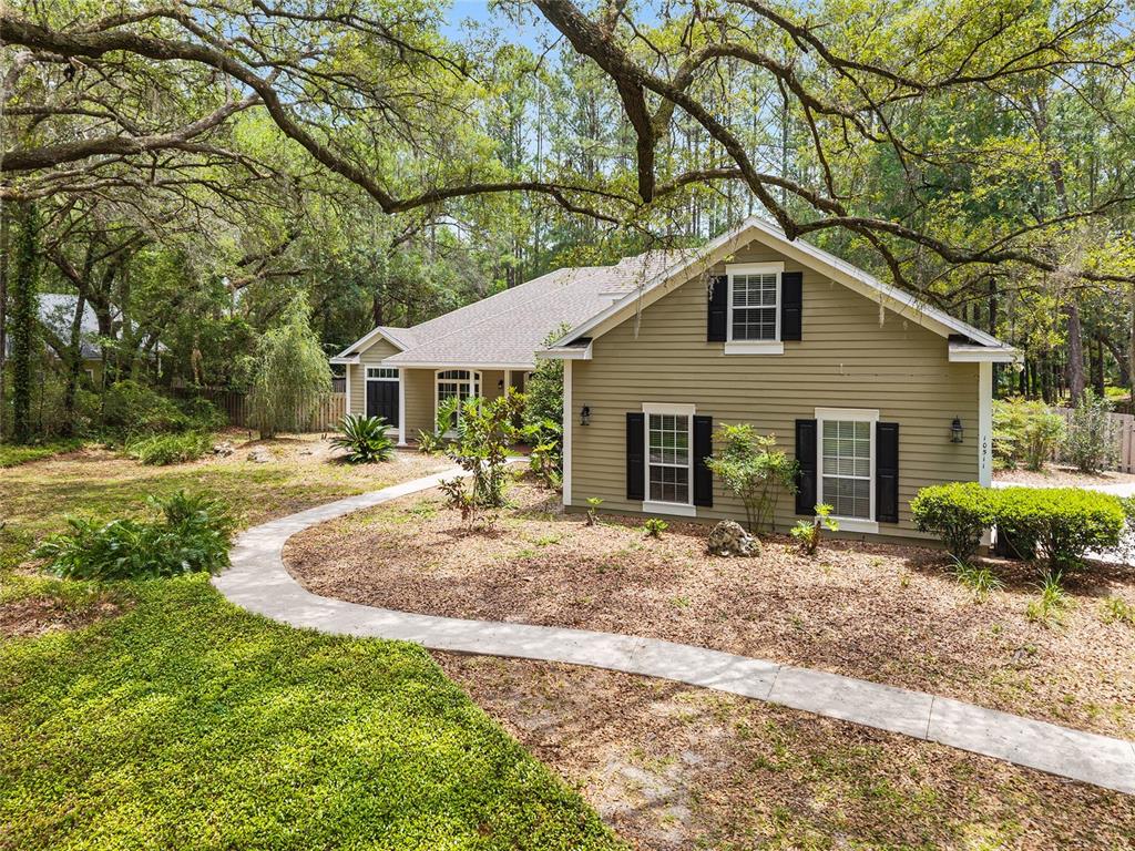 A single-story house with olive green siding and black shutters sits behind a curved walkway — 10511 SW 17TH PLACE, GAINESVILLE, FL