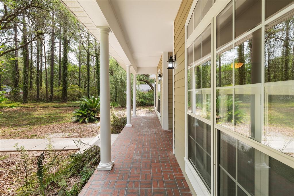 A covered brick porch with white columns runs alongside a house with large windows — 10511 SW 17TH PLACE, GAINESVILLE, FL