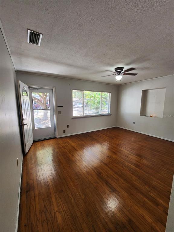 An empty living room features hardwood floors, a ceiling fan, and a glass-paneled entry door — 1608 EDNA AVENUE, LARGO, FL
