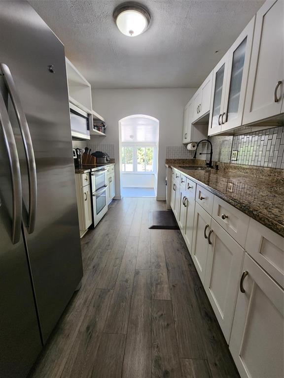 A galley kitchen features white cabinets, granite countertops, stainless steel appliances, and wood-look flooring — 1608 EDNA AVENUE, LARGO, FL