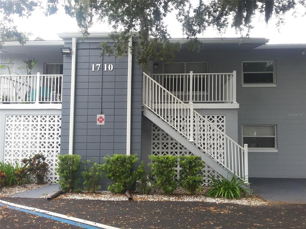 A two-story apartment building exterior features gray block walls, white railings, and a staircase — 1710 S WASHINGTON AVENUE UNIT 14, TITUSVILLE, FL