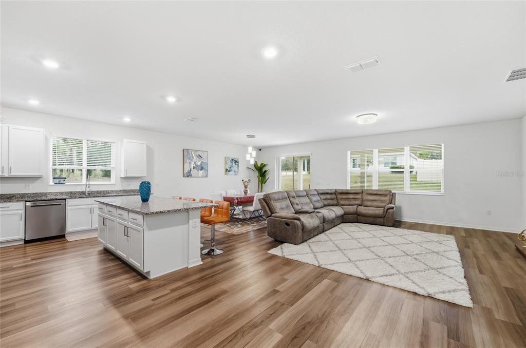 An open-concept kitchen, dining area, and living room with wood-look flooring and a sectional sofa — 2081 MALBEC COURT, MINNEOLA, FL