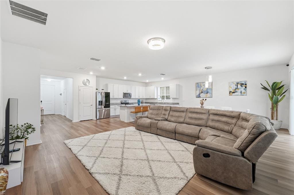 An open-concept living room features a large sectional sofa, a white rug, and a kitchen — 2081 MALBEC COURT, MINNEOLA, FL