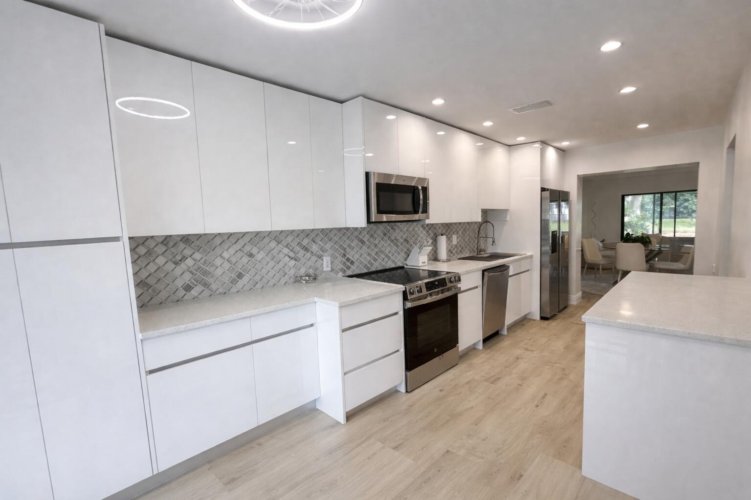 A modern kitchen features white flat-panel cabinets, stainless steel appliances, and a gray tiled backsplash — 4 Westgate Lane # 4c, Boynton Beach FL 33436, BOYNTON BEACH, FL