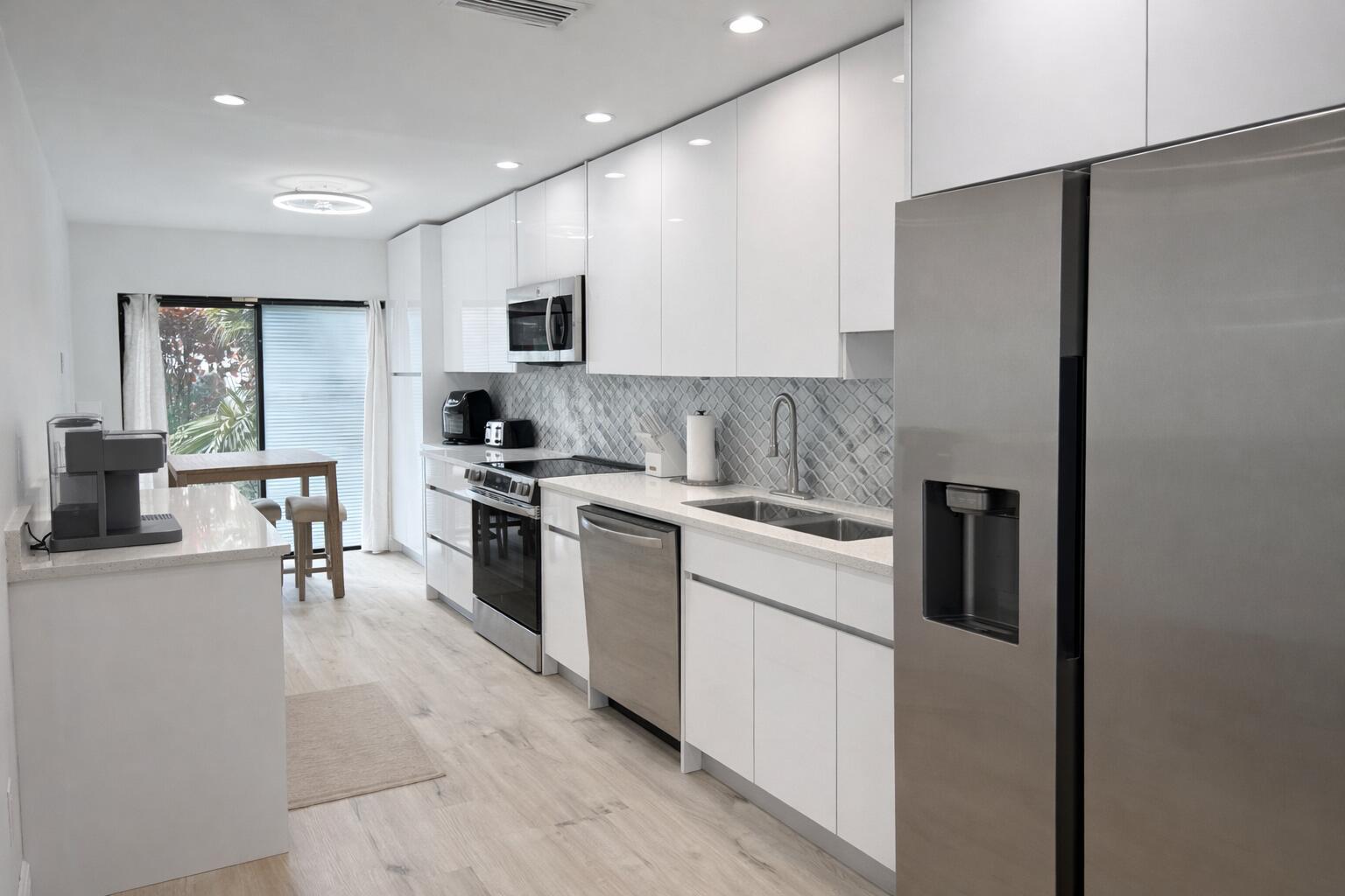 A modern kitchen features white flat-panel cabinets, stainless steel appliances, and a gray patterned backsplash — 4 Westgate Lane # 4c, Boynton Beach FL 33436, BOYNTON BEACH, FL