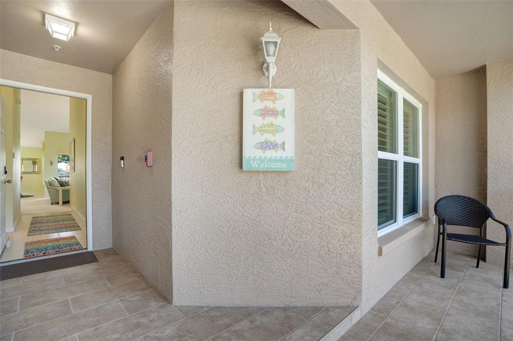 A covered patio features tiled flooring, a textured wall with a fish-themed sign, and seating — 5310 HYLAND HILLS AVENUE UNIT 2124, SARASOTA, FL