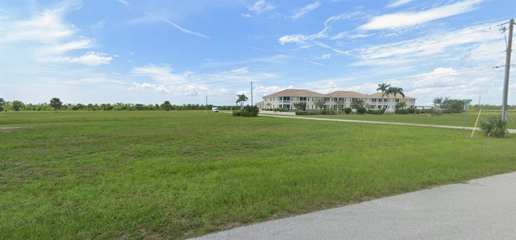 A large, flat, grassy vacant lot with a multi-story apartment building in the background — 17170 BARCREST LANE, PUNTA GORDA, FL