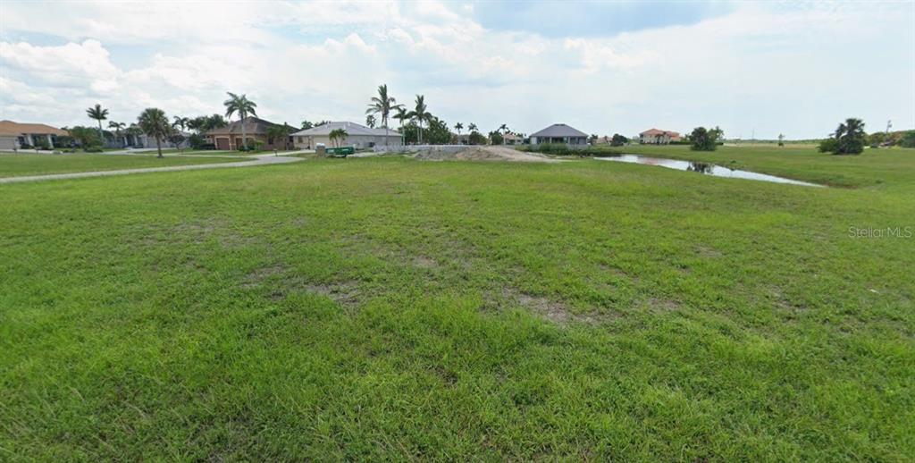 A large, grassy vacant lot features a small pond and distant houses under a cloudy sky — 17170 BARCREST LANE, PUNTA GORDA, FL