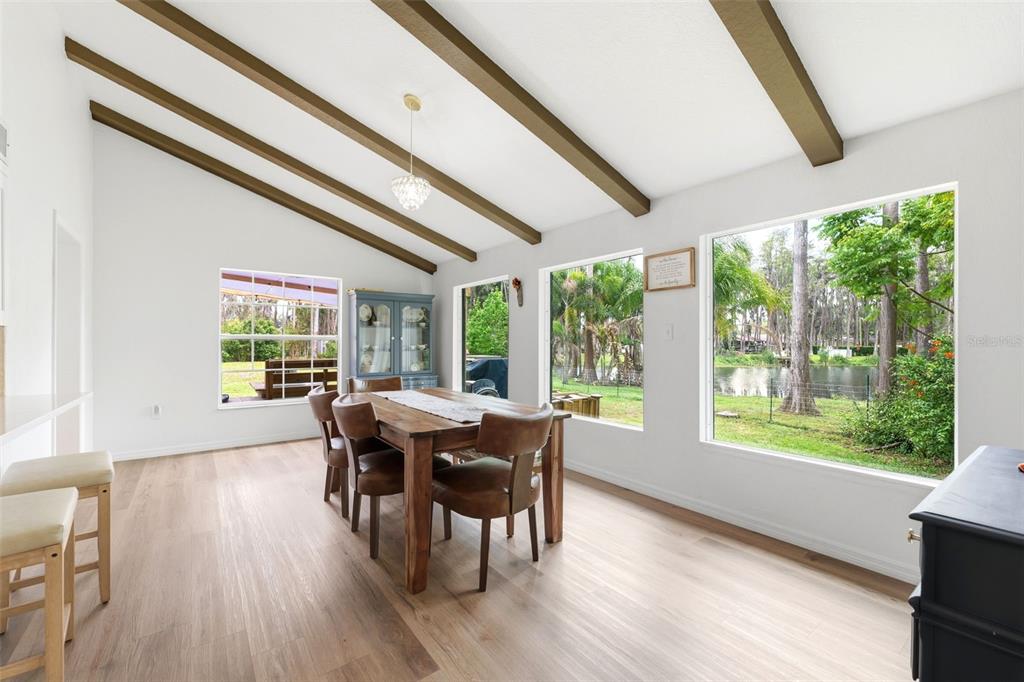 A dining room with vaulted ceilings, exposed beams, and large windows overlooking a backyard pond — 19003 CEDAR LANE, LUTZ, FL