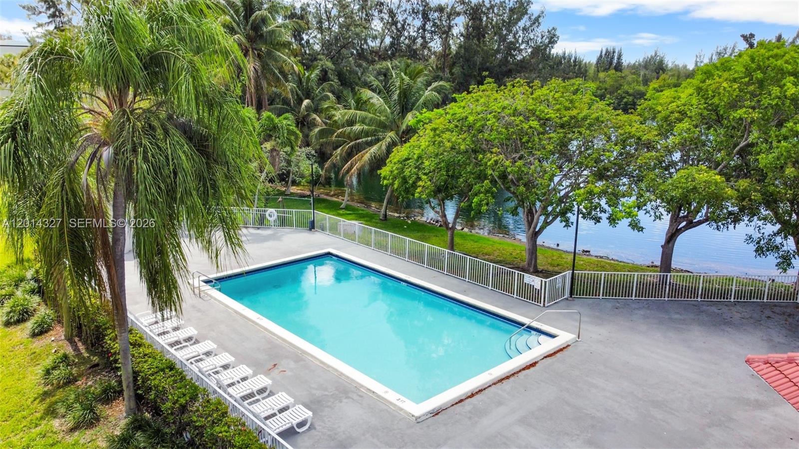 An outdoor swimming pool is surrounded by a concrete deck, white fencing, and lush trees — 8200 SW 210th St # 103, Cutler Bay FL 33189, CUTLER BAY, FL
