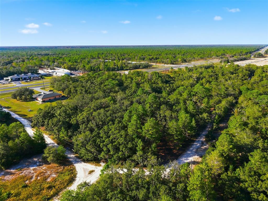 An aerial view shows a wooded lot with dirt roads and nearby commercial buildings — 11254 COMMERCIAL WAY, WEEKI WACHEE, FL