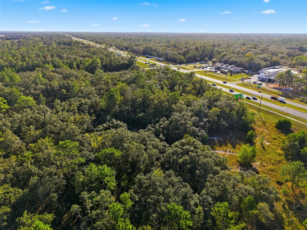 An aerial view shows a wooded lot adjacent to a highway with commercial buildings nearby — 11254 COMMERCIAL WAY, WEEKI WACHEE, FL