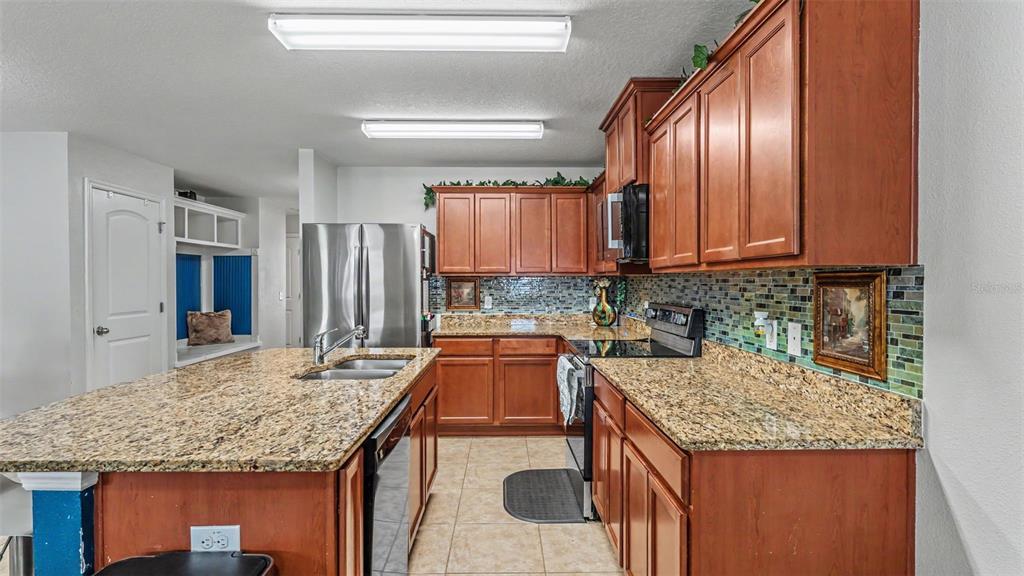 A kitchen features wood cabinets, granite countertops, a center island, and a mosaic tile backsplash — 5739 LACAR WAY, LAKELAND, FL