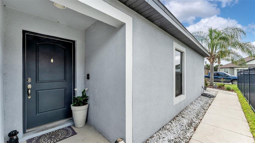 A gray front door with a side light sits beside a potted plant and walkway — 5739 LACAR WAY, LAKELAND, FL