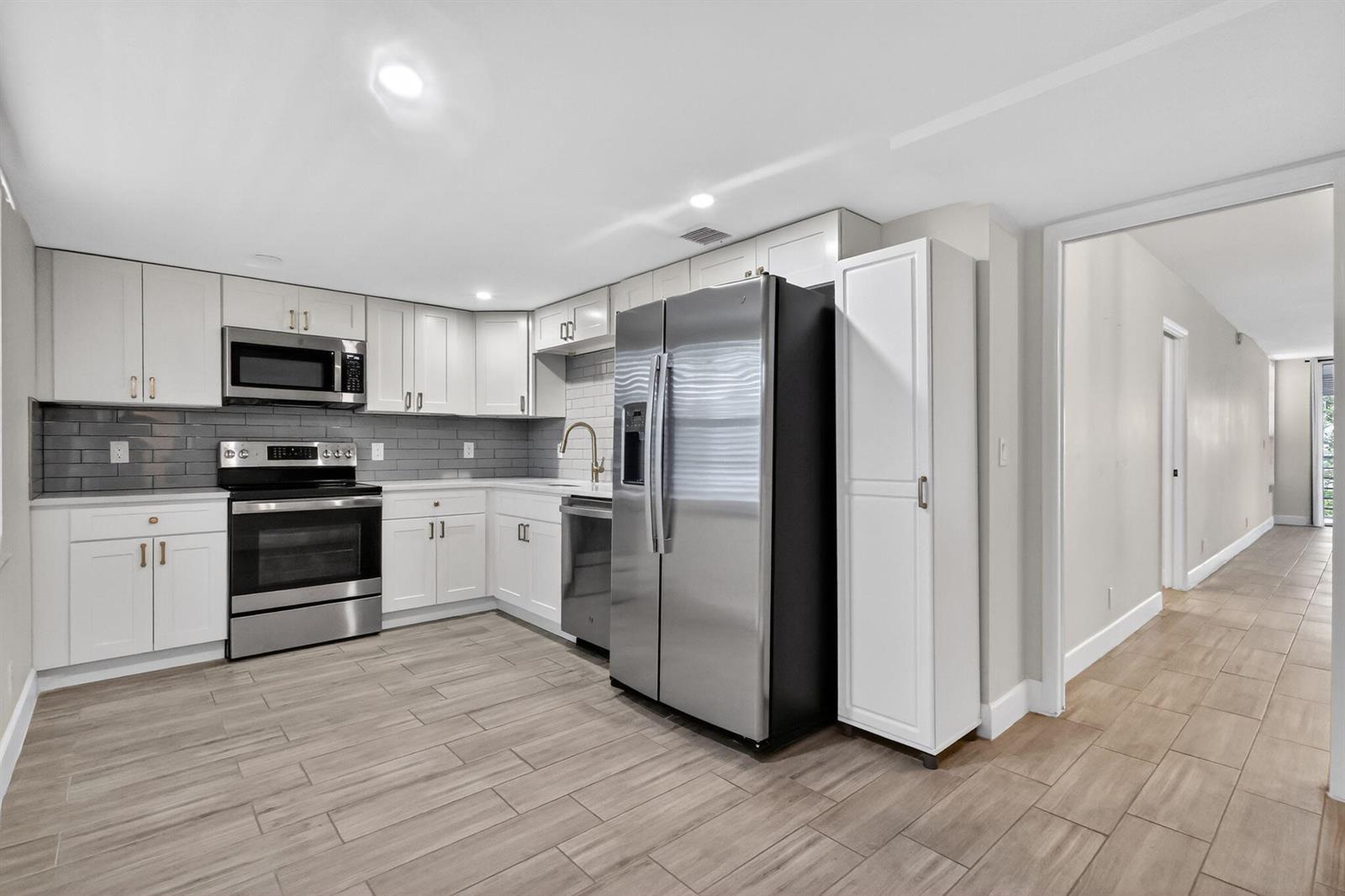 A kitchen with white cabinets, stainless steel appliances, gray subway tile backsplash, and wood-look flooring — 545 Oaks Lane # 409, Pompano Beach FL 33069, POMPANO BEACH, FL