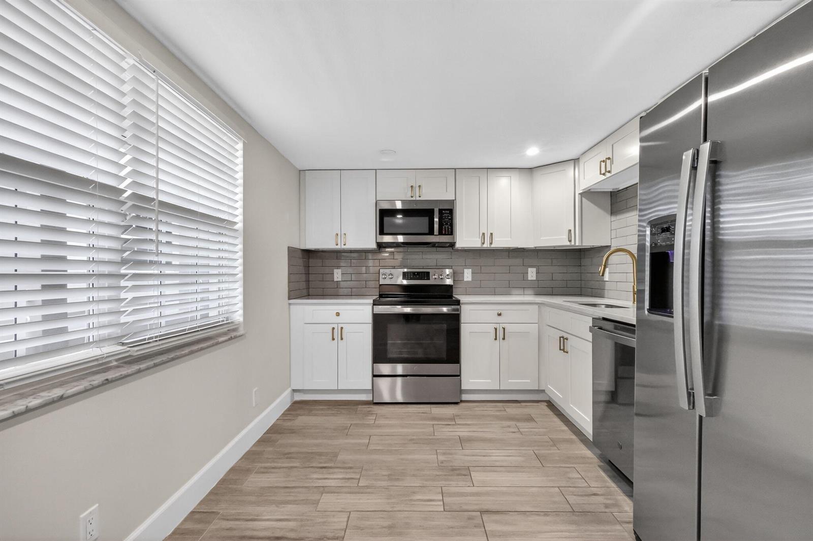 A kitchen with white cabinets, stainless steel appliances, gray subway tile backsplash, and wood-look flooring — 545 Oaks Lane # 409, Pompano Beach FL 33069, POMPANO BEACH, FL
