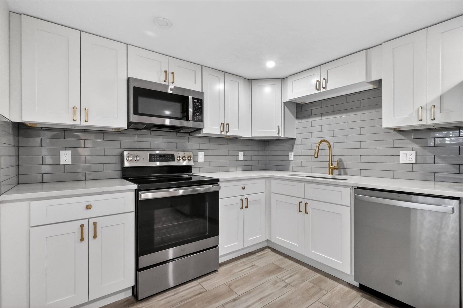 A kitchen with white cabinets, stainless steel appliances, gray subway tile backsplash, and wood-look flooring — 545 Oaks Lane # 409, Pompano Beach FL 33069, POMPANO BEACH, FL