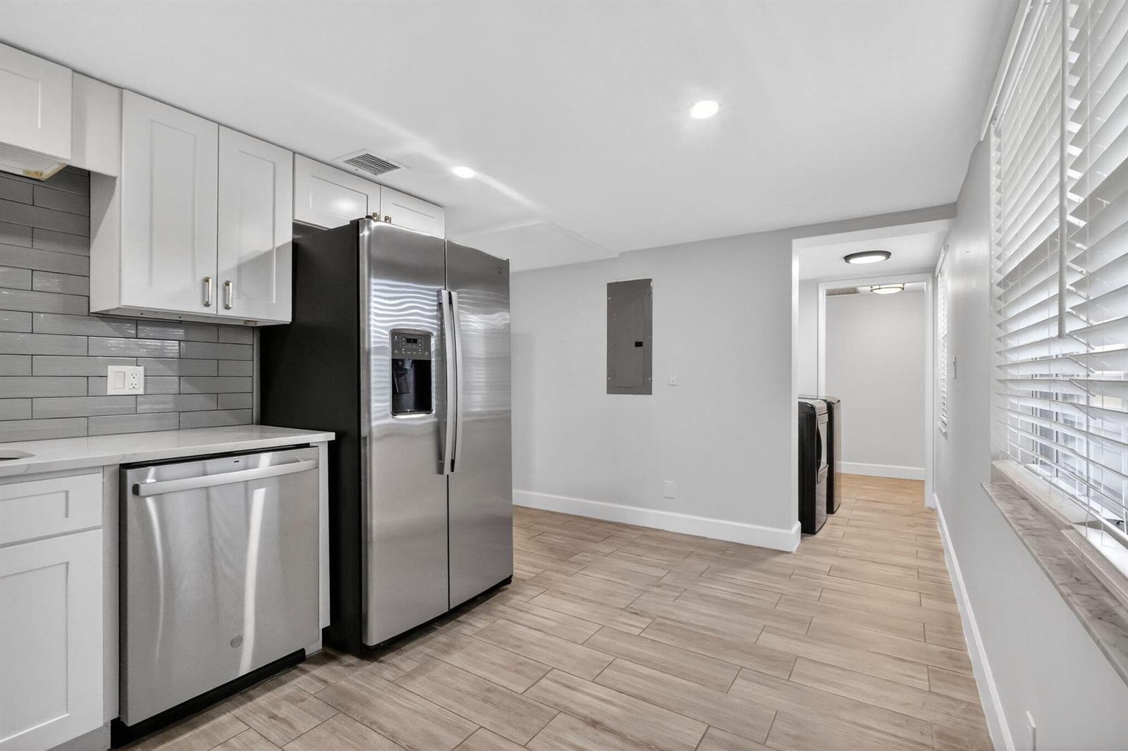 A kitchen with white cabinets, stainless steel appliances, gray subway tile, and wood-look tile flooring — 545 Oaks Lane # 409, Pompano Beach FL 33069, POMPANO BEACH, FL