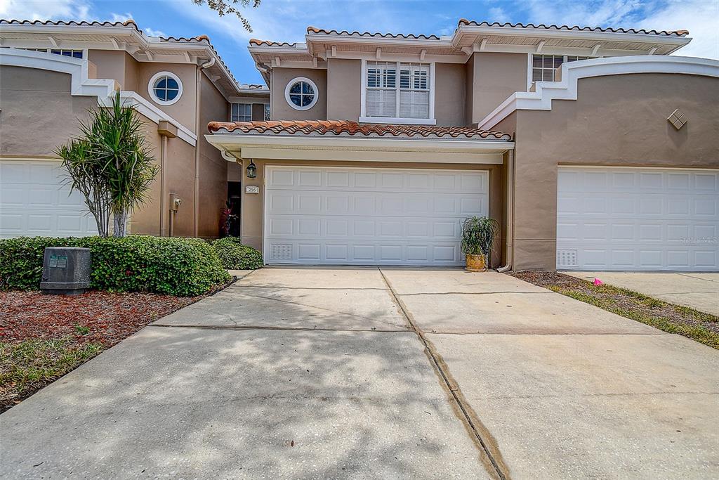 A two-story townhouse exterior features a white garage door, a concrete driveway, and tiled roofing — 256 VALENCIA CIRCLE, ST PETERSBURG, FL