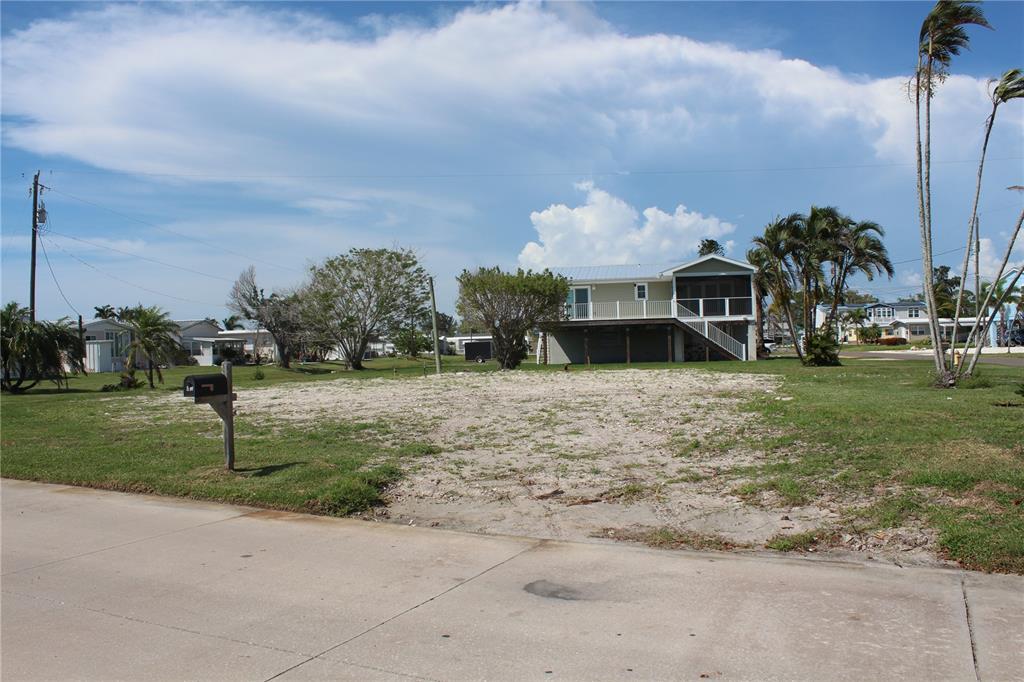 A vacant, sandy residential lot sits in front of an elevated house with palm trees — 10315 CORTEZ ROAD W UNIT 1/2 BV, BRADENTON, FL