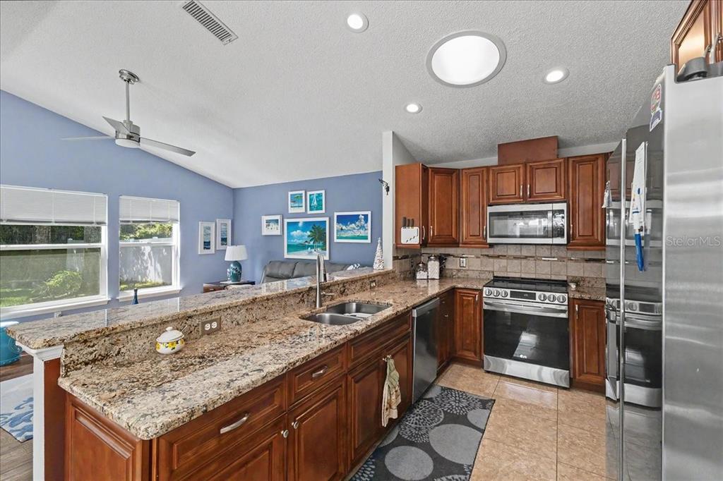 A kitchen features granite countertops, wood cabinets, stainless steel appliances, and a vaulted ceiling — 47 CARRIAGE CREEK WAY, ORMOND BEACH, FL