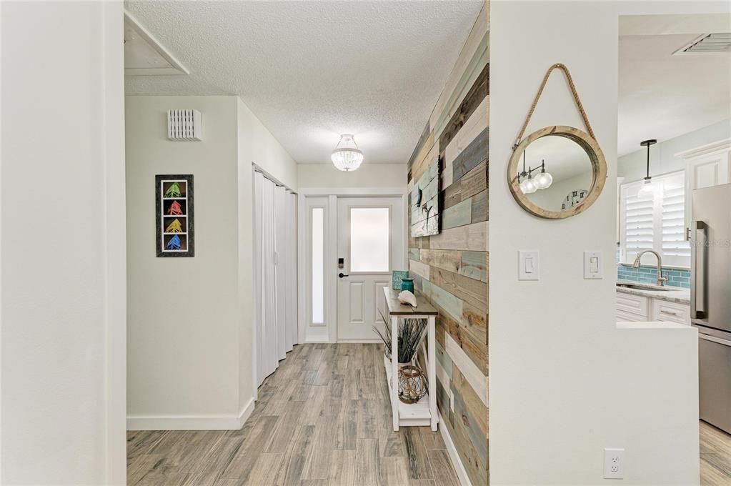 An entryway features wood-plank accent wall, wood-look tile flooring, a round mirror, and white doors — 1218 MOONMIST CIRCLE UNIT S2, SARASOTA, FL
