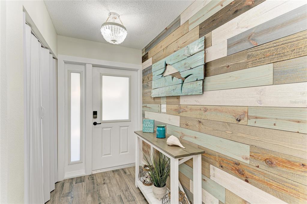 An entryway features a wood-plank accent wall, a white front door, and a console table — 1218 MOONMIST CIRCLE UNIT S2, SARASOTA, FL