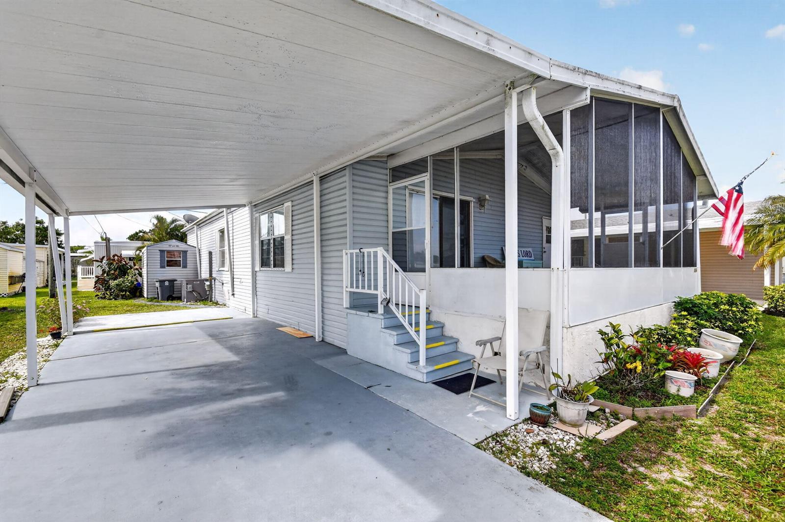 A light blue mobile home features a covered carport, screened porch, and front steps — 4290 Meadow View Drive, Boynton Beach FL 33436, BOYNTON BEACH, FL