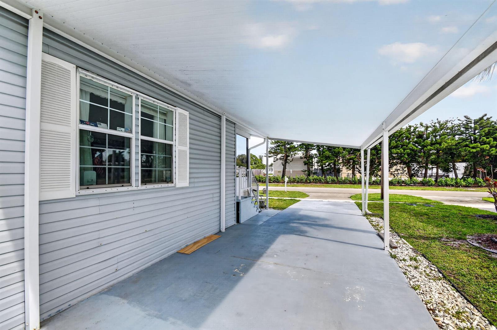 A covered concrete carport sits beside the light gray vinyl siding of a mobile home — 4290 Meadow View Drive, Boynton Beach FL 33436, BOYNTON BEACH, FL