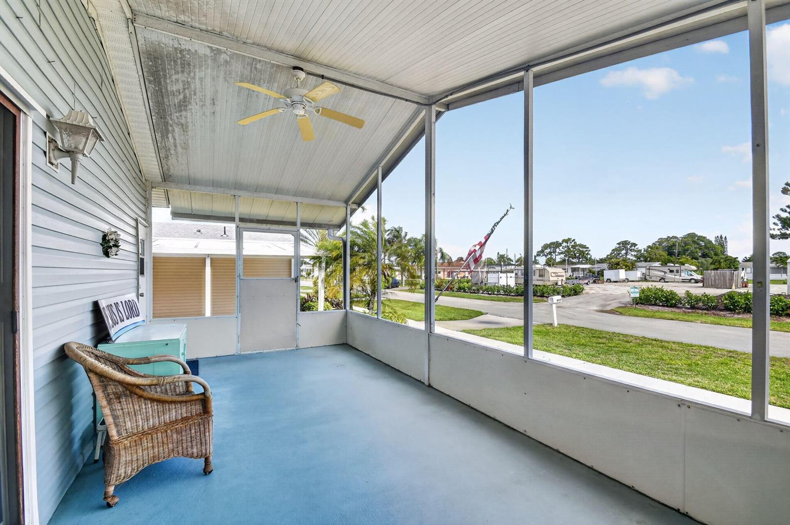 A screened-in porch with a blue floor, ceiling fan, and wicker chair overlooks a street — 4290 Meadow View Drive, Boynton Beach FL 33436, BOYNTON BEACH, FL