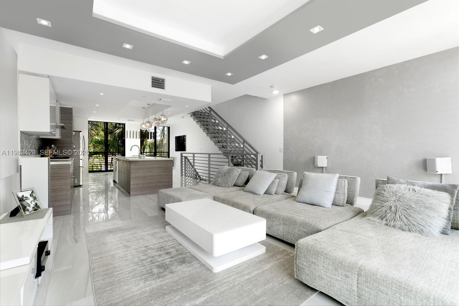 A modern open-concept living room and kitchen featuring gray sectional seating and a staircase — 1065 99th St, Bay Harbor Islands FL 33154, BAY HARBOR ISLANDS, FL