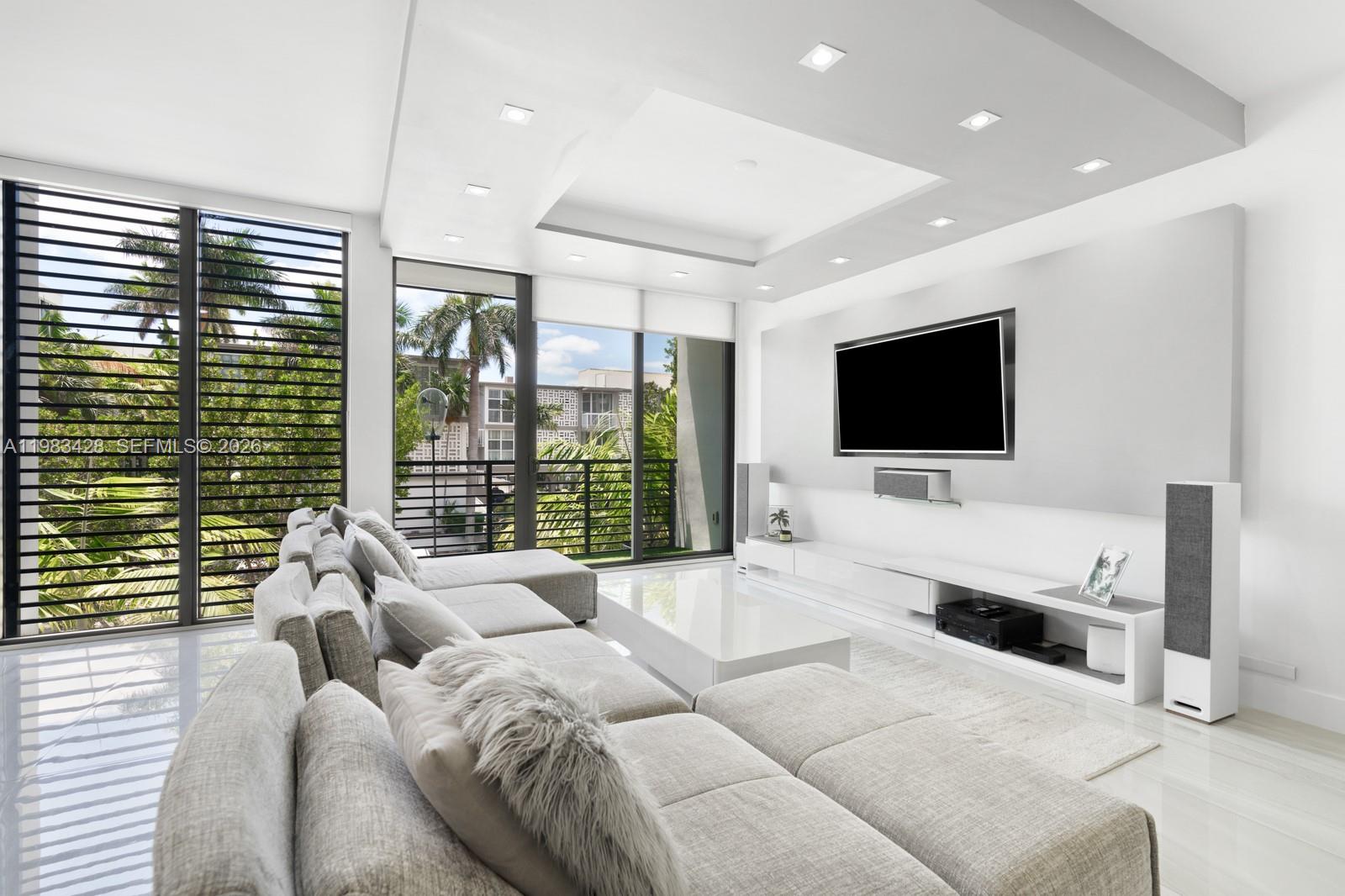 A modern living room features a large sectional sofa, a wall-mounted television, and floor-to-ceiling windows — 1065 99th St, Bay Harbor Islands FL 33154, BAY HARBOR ISLANDS, FL