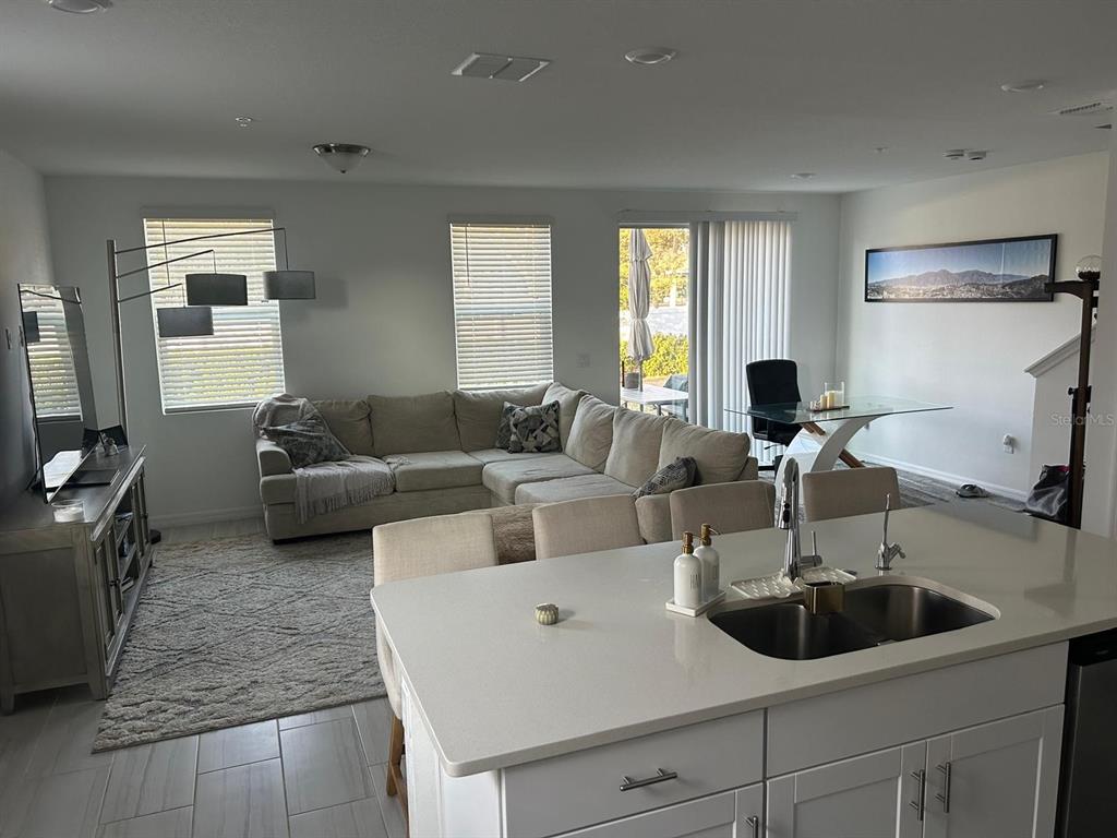 A kitchen island with a double sink overlooks an open-concept living room with a sectional — 2037 CRAPE JASMINE LANE, ORLANDO, FL