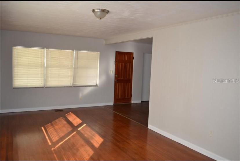 An empty living room features hardwood floors, light gray walls, and a large window with blinds — 609 S MONTGOMERY AVENUE, DELAND, FL