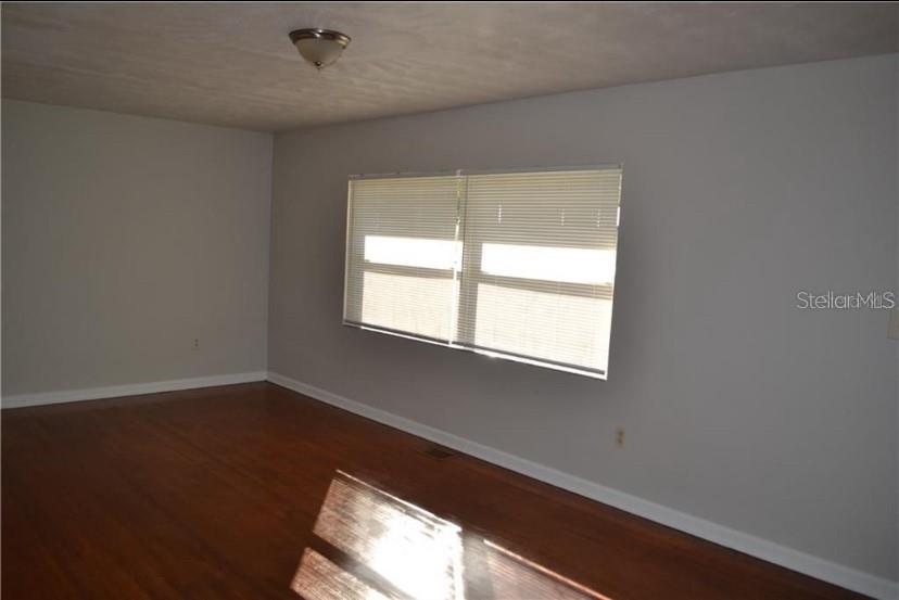 An empty room with hardwood flooring, light gray walls, and a window with white blinds — 609 S MONTGOMERY AVENUE, DELAND, FL