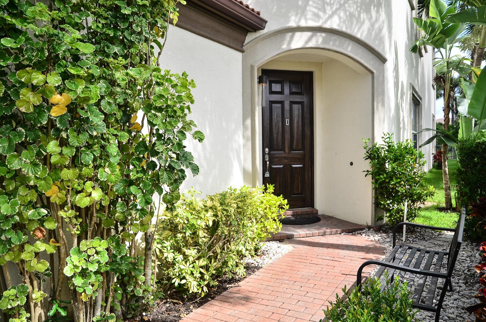 A brick walkway leads to a dark wood front door under a stucco archway — 9720 Phipps Lane, Wellington FL 33414, WELLINGTON, FL