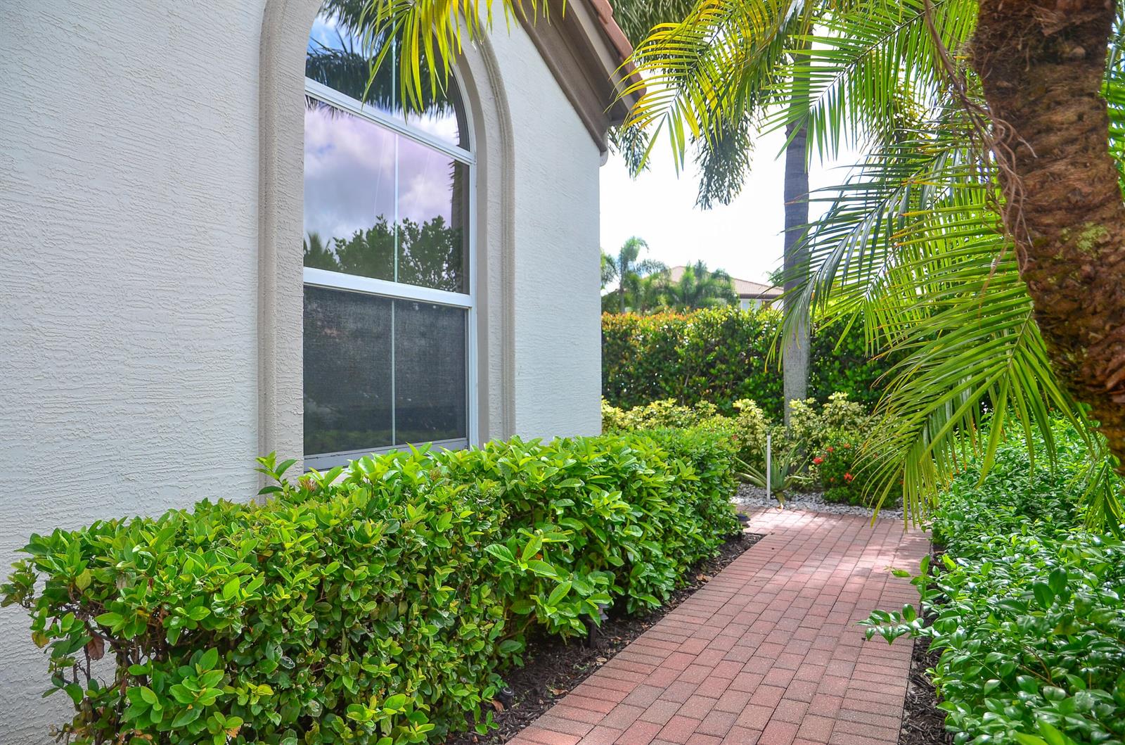 A brick walkway leads past a white stucco house wall with an arched window — 9720 Phipps Lane, Wellington FL 33414, WELLINGTON, FL