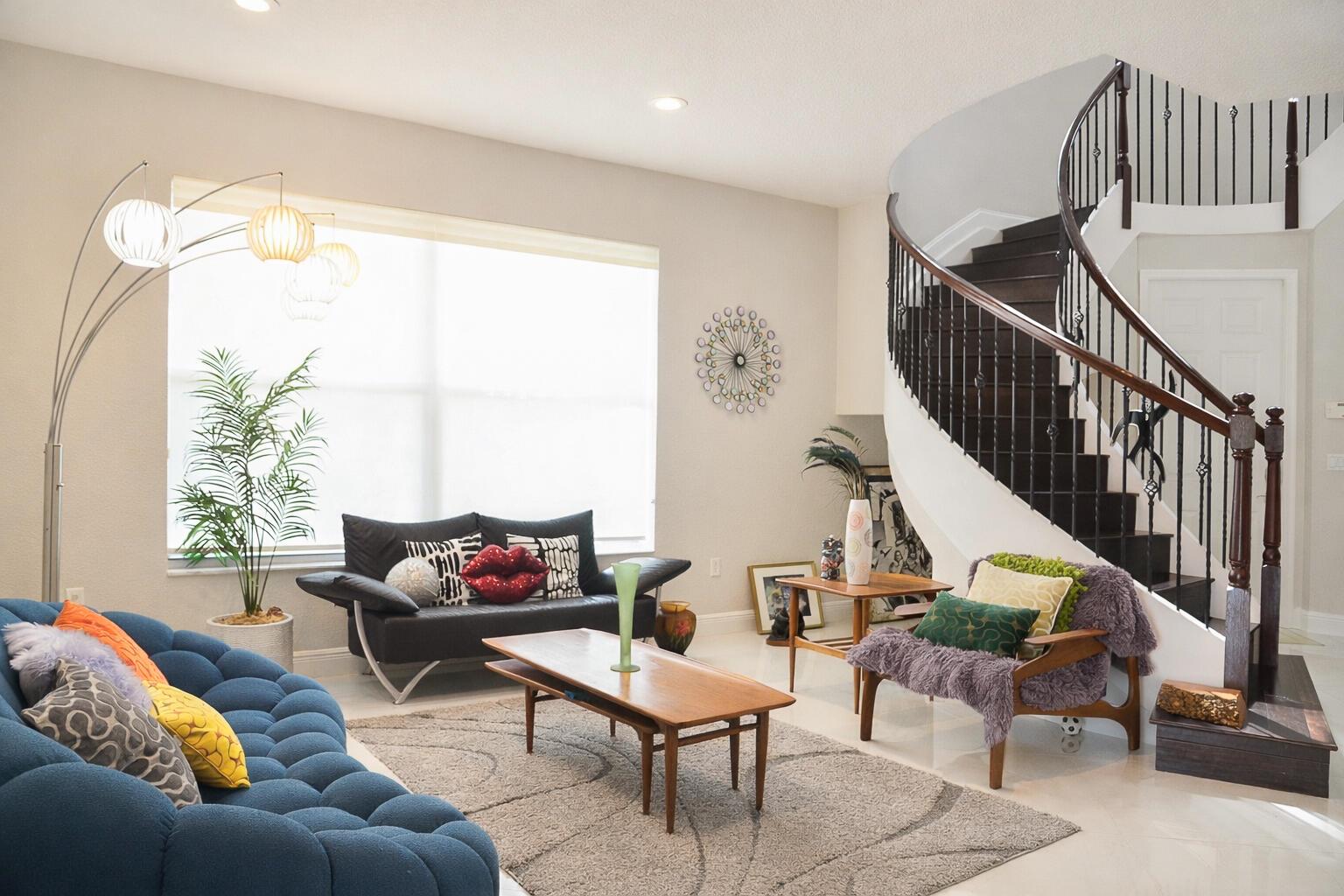 A living room features a curved staircase, a blue tufted sofa, and a coffee table — 9720 Phipps Lane, Wellington FL 33414, WELLINGTON, FL
