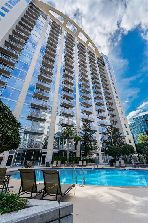 A tall modern apartment building with glass balconies overlooks a swimming pool and patio area — 155 S COURT AVENUE UNIT 2403, ORLANDO, FL