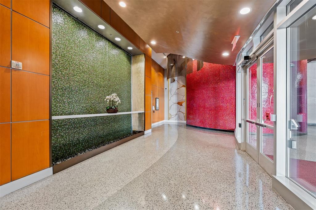 A modern lobby features a green mosaic water wall, a red accent wall, and terrazzo flooring — 155 S COURT AVENUE UNIT 2403, ORLANDO, FL