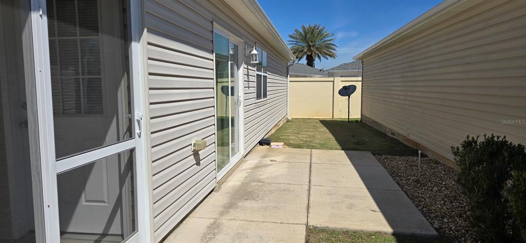 A concrete patio sits between the side of a house and a neighboring wall — 1009 RIDGEVILLE ROAD, THE VILLAGES, FL