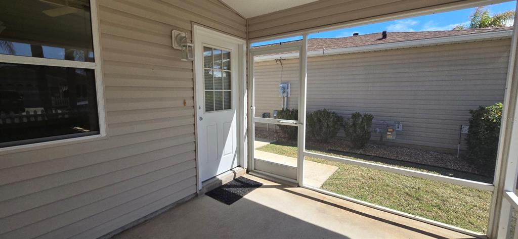A screened-in porch features a white door, concrete flooring, and vinyl siding — 1009 RIDGEVILLE ROAD, THE VILLAGES, FL