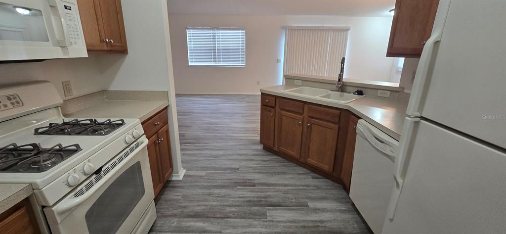 A kitchen with wood cabinets, white appliances, and light-colored flooring opens to a living area — 1009 RIDGEVILLE ROAD, THE VILLAGES, FL
