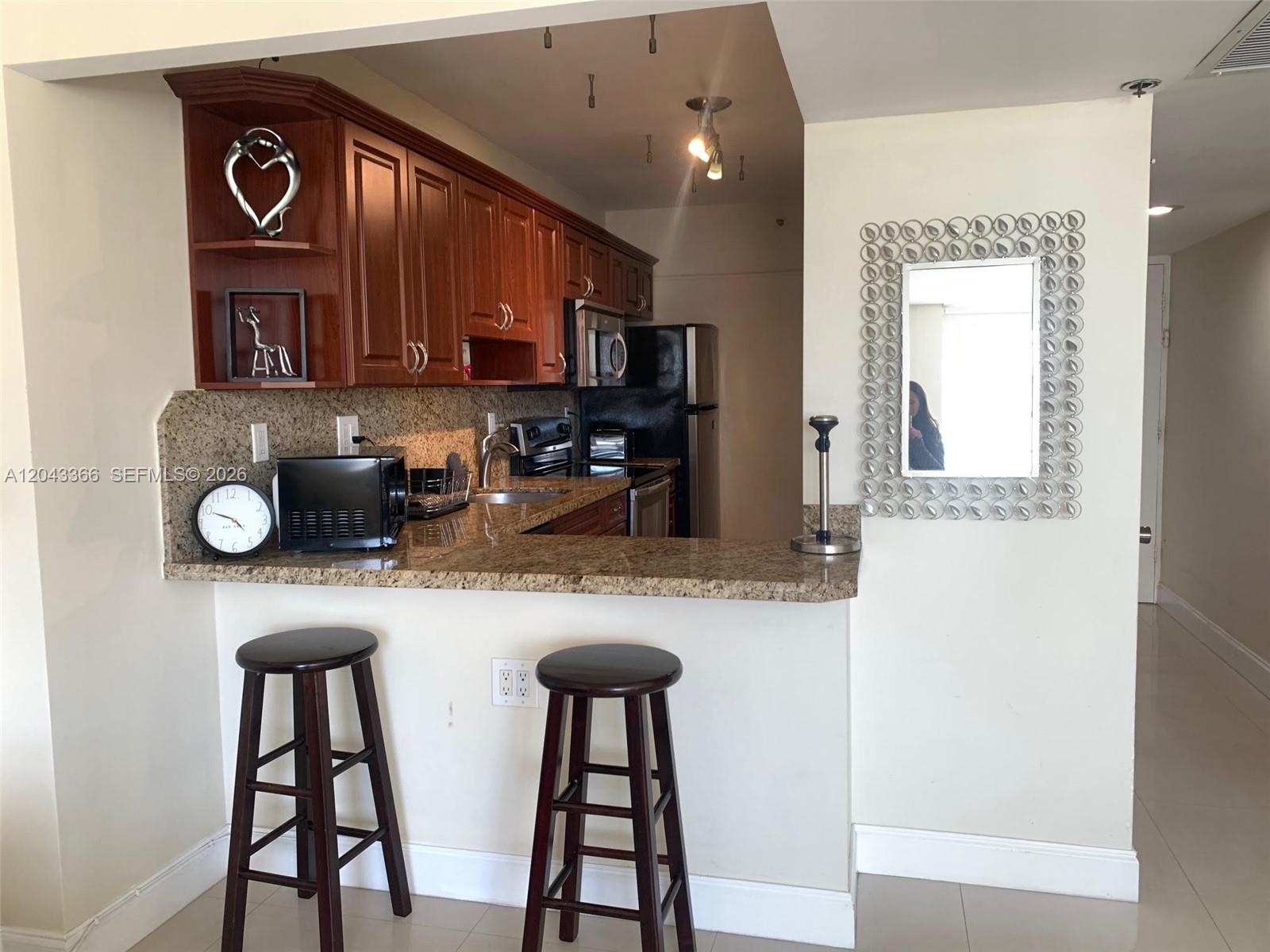 A kitchen features wood cabinets, granite countertops, a breakfast bar with stools, and a mirror — 100 Lincoln Rd # 316, Miami Beach FL 33139, MIAMI BEACH, FL