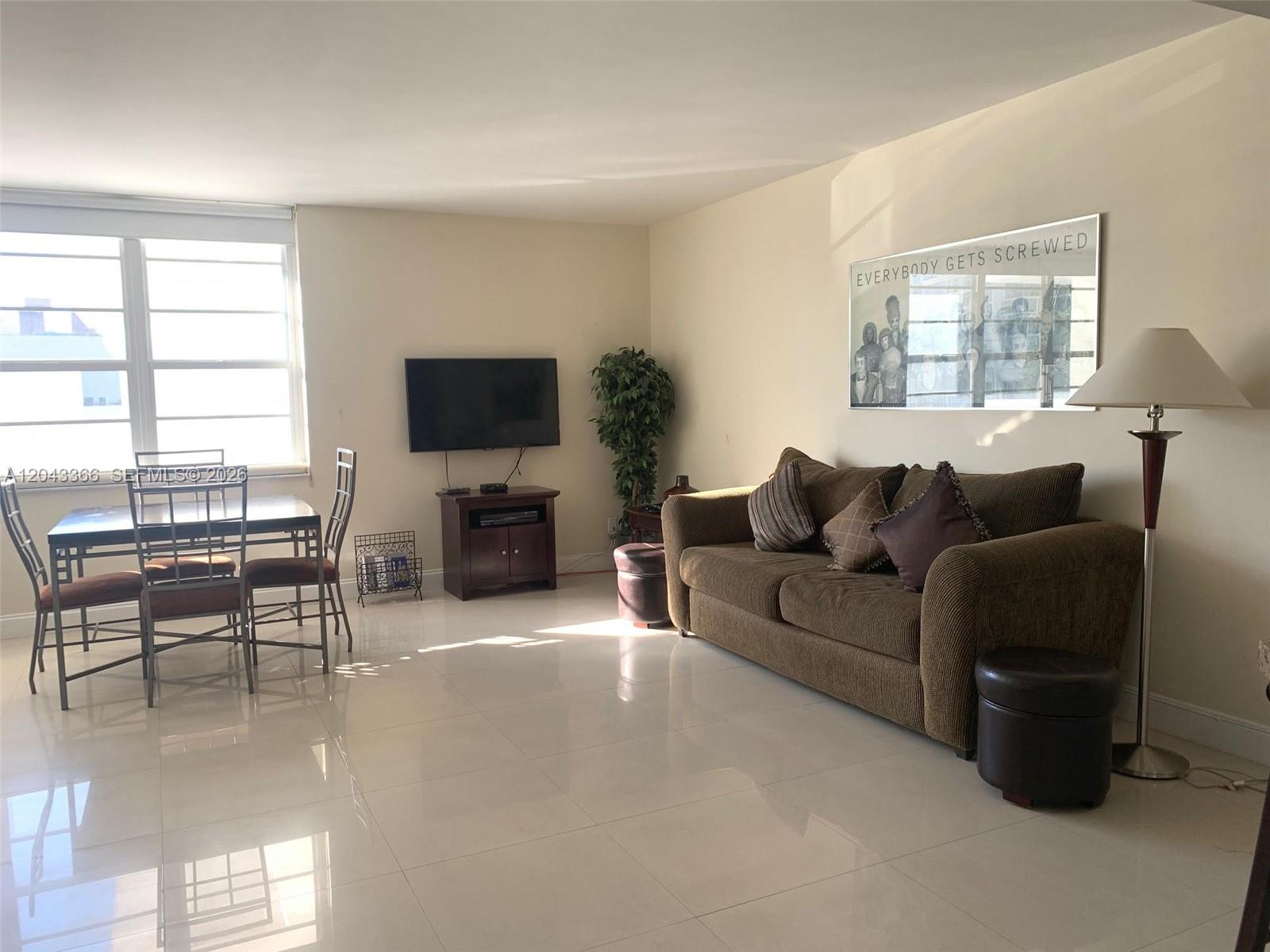 A living room with a brown sofa, dining set, tile flooring, and a wall-mounted television — 100 Lincoln Rd # 316, Miami Beach FL 33139, MIAMI BEACH, FL