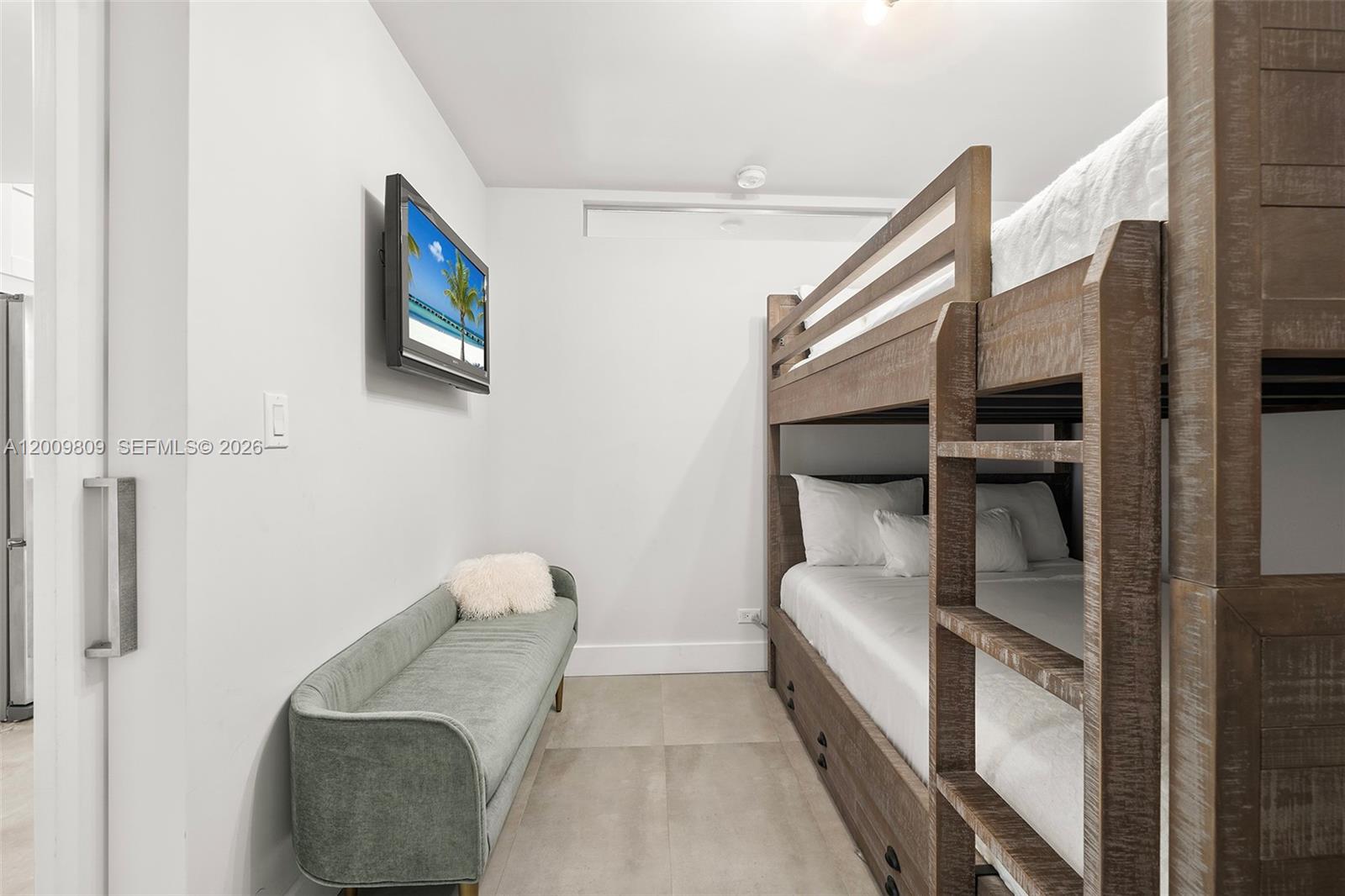 A bedroom features a wooden bunk bed, a green bench, and a wall-mounted television — 2301 Collins Ave # 1533, Miami Beach FL 33139, MIAMI BEACH, FL