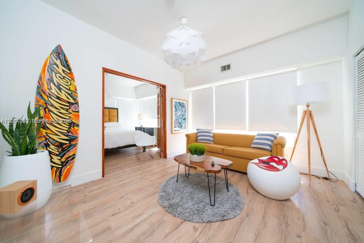 A living room features a yellow sofa, a surfboard, and a wooden coffee table — 227 1st St # 7, Miami Beach FL 33139, MIAMI BEACH, FL