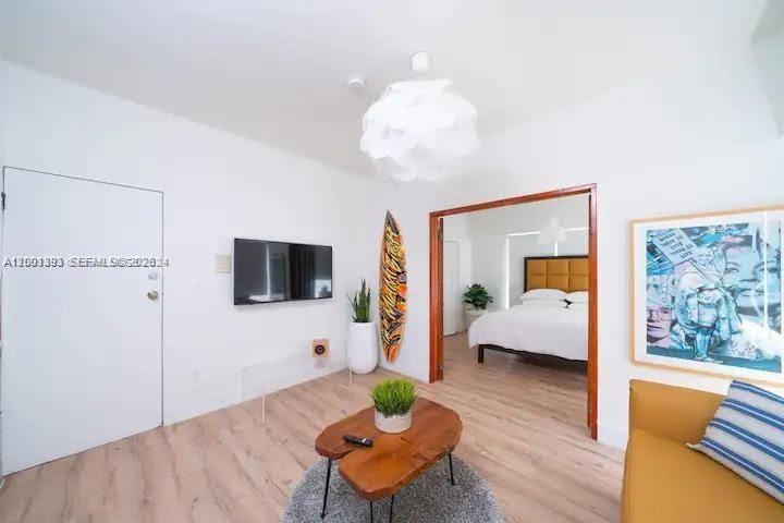 A living room with light wood floors, a surfboard, and a view into a bedroom — 227 1st St # 7, Miami Beach FL 33139, MIAMI BEACH, FL